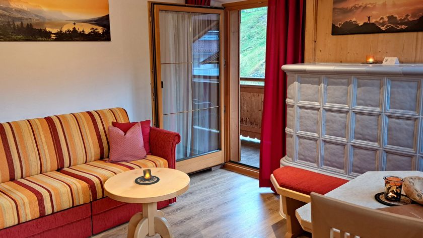 Wohnbereich im Appartement Großer Beil mit Sofa, Kachelofen und Zugang zum Balkon