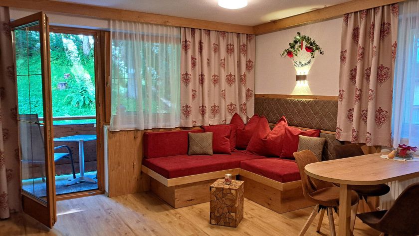 Wohnbereich im Appartement Gratlspitz mit roter Eckbank, Esstisch und Balkon
